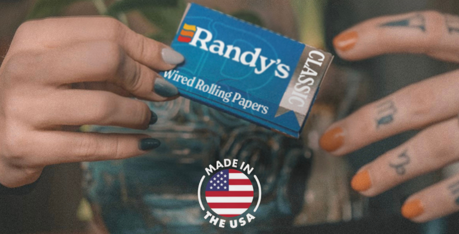 Person passing a pack of Randy's Classic Wired Rolling Papers with 'Made in the USA' logo displayed.