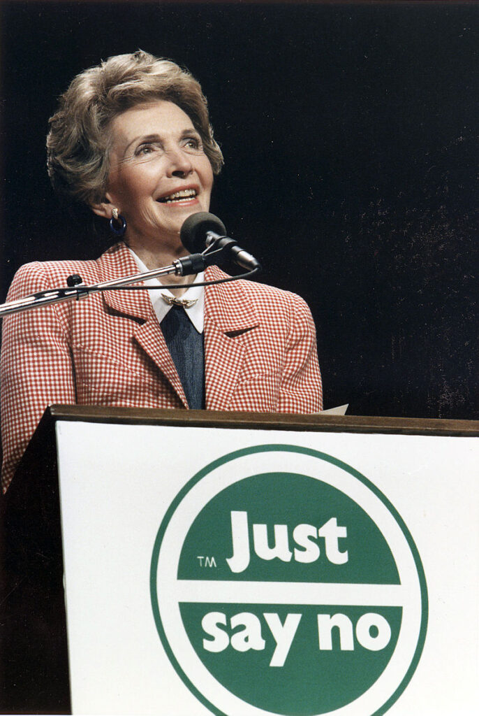 "Nancy Reagan speaking at a podium with a 'Just Say No' campaign logo during an anti-drug rally."