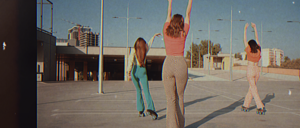 Three members of Randy’s community roller skating outdoors in a sunny urban setting. They wear colorful, retro-inspired outfits, raising their arms as they skate away, reflecting a carefree and connected lifestyle.